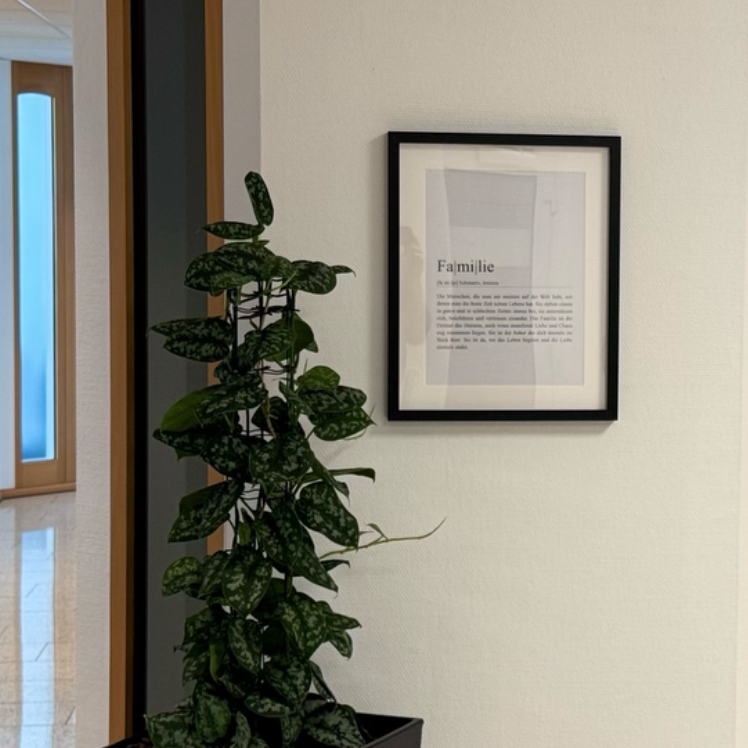 Ein gerahmter Text hängt an einer Wand neben einer Pflanze in einem modernen Raum.