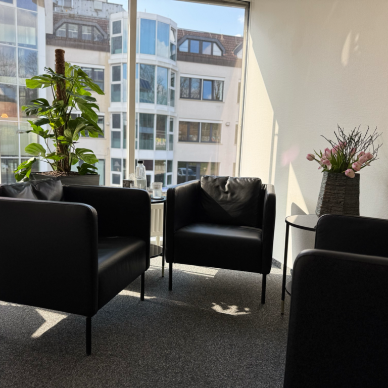 Zwei Puppen sitzen in schwarzen Sesseln um einen kleinen Tisch.