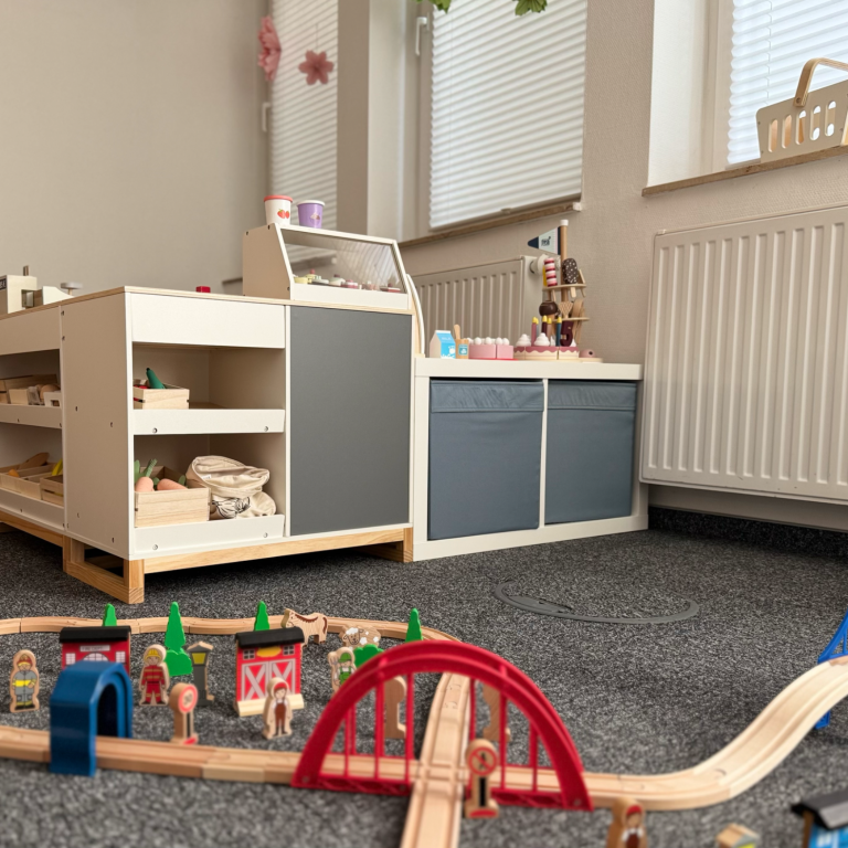 Spielzimmer mit Holzspielzeug, Eisenbahntrasse und niedrigen Regalen.