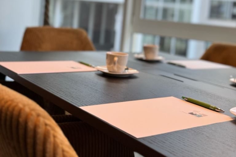 Besprechungstisch mit Notizblöcken, Stiften und Kaffeetassen.