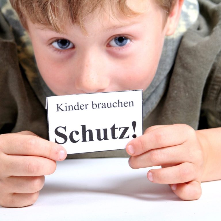 Ein Kind hält ein Schild mit der Aufschrift "Kinder brauchen Schutz!"