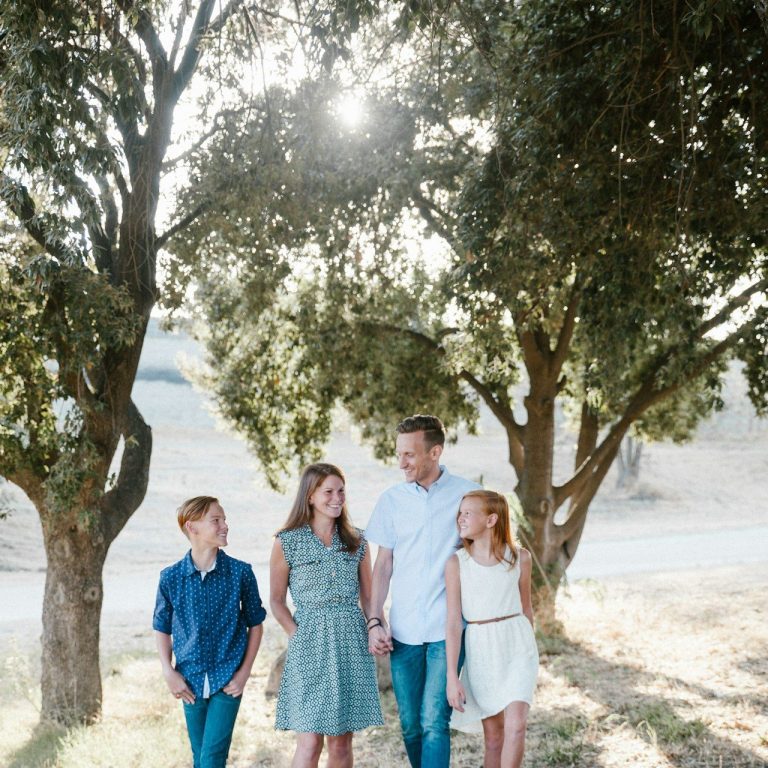 Familie steht zusammen unter Bäumen in einer sonnigen, ländlichen Umgebung.